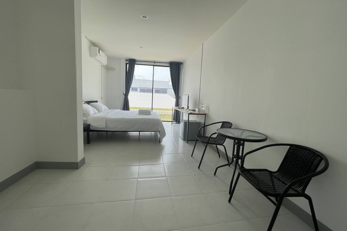 A hotel room with a bed, a desk, two chairs, and a large window with curtains.