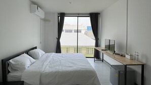 Habitación de hotel moderna con cama, escritorio, televisor y vistas al balcón.