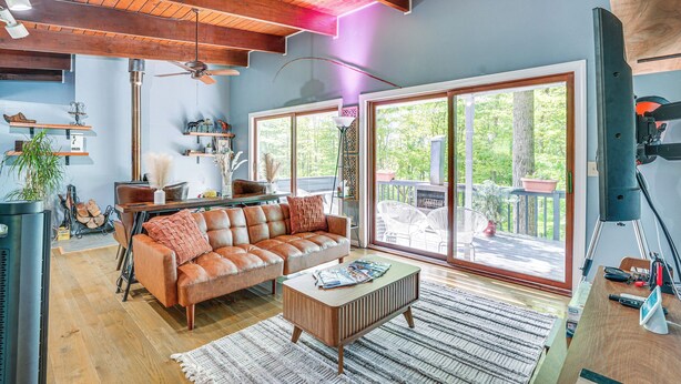 A spacious living room with a large window, a wooden ceiling, and a leather sofa. - 'Alpine House' Modern Delevan Cabin on 2 Acres (Delevan)
