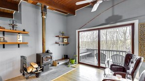 A spacious living room with a fireplace, wooden floors, and a large sliding glass door leading to an outdoor deck. - 'Alpine House' Modern Delevan Cabin on 2 Acres (Delevan)