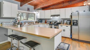 A modern kitchen with white cabinets, a wooden ceiling, and a large island with bar stools. - 'Alpine House' Modern Delevan Cabin on 2 Acres (Delevan)