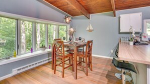 A dining area with a wooden table, chairs, and a view of trees through large windows. - 'Alpine House' Modern Delevan Cabin on 2 Acres (Delevan)