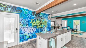 A modern kitchen with a central island, a teal accent wall, and a graffiti-style mural.