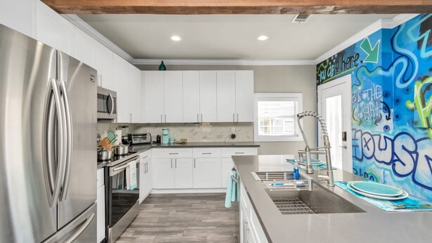A modern kitchen with stainless steel appliances, white cabinetry, and a graffiti wall.