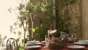 A round table set for dining outdoors with plates, glasses, and a basket of bread.