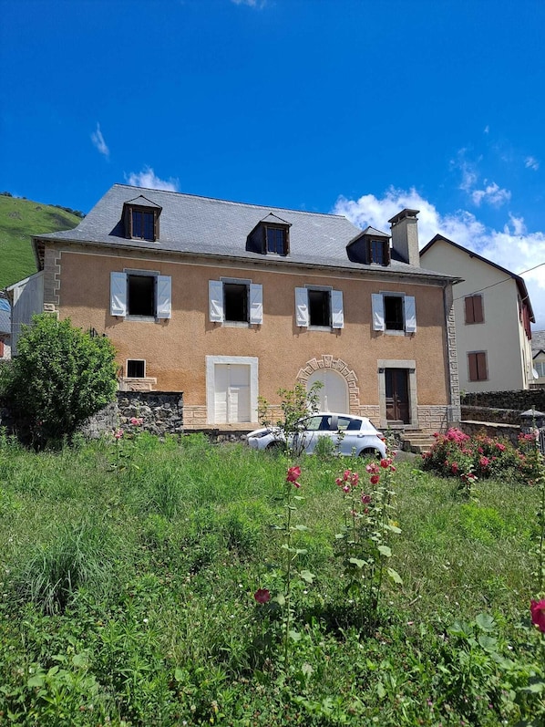 A two-story house with a stone facade, a central entrance, and a car parked in front.