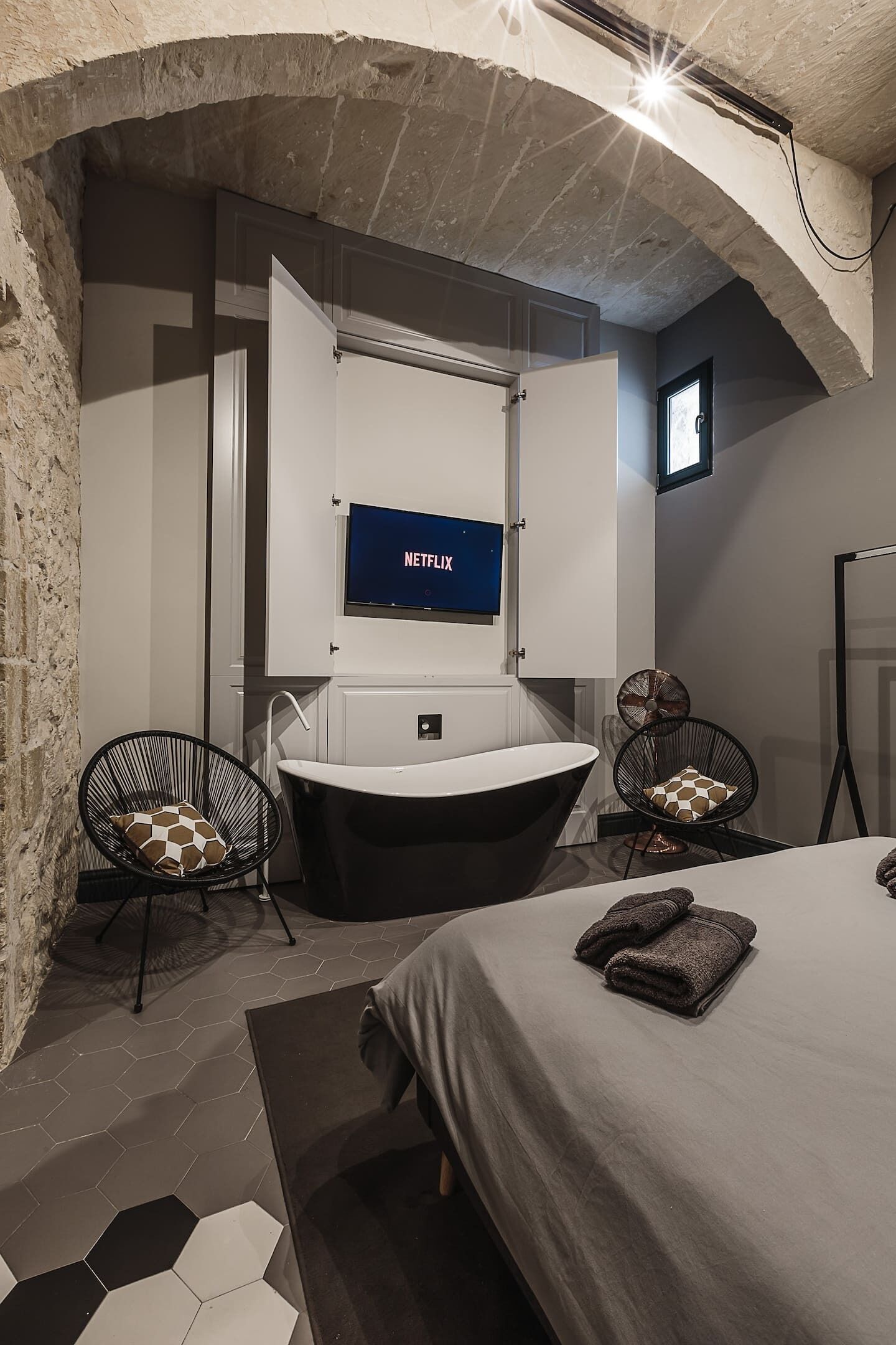 A modern bathroom with a freestanding bathtub, a large mirror, and a mounted television displaying Netflix.