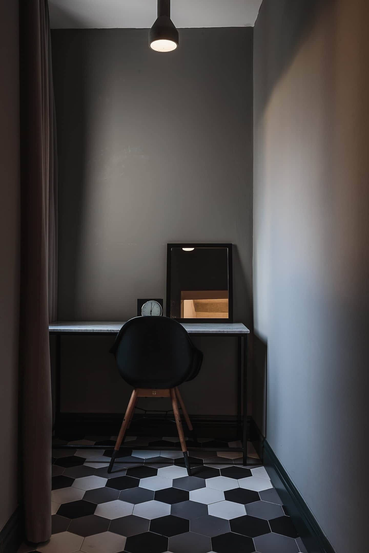 A small, dimly lit room with a desk, chair, and a clock on the wall.