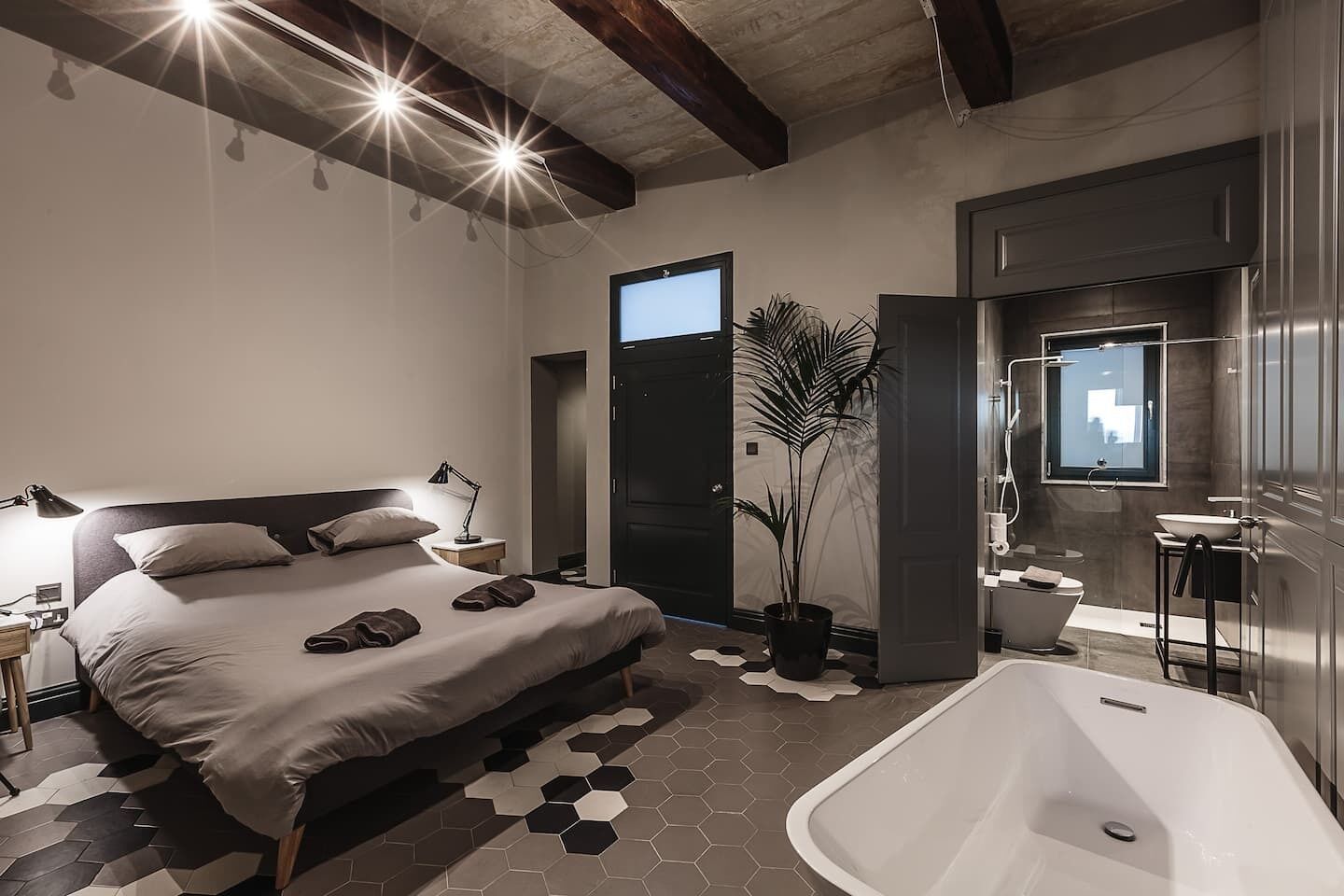 A modern bedroom with a large bed, bedside table, lamp, and a potted plant.