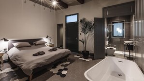 Ein modernes Schlafzimmer mit einem großen Bett, Nachttisch, Lampe und einer Topfpflanze.