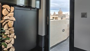 Ein modernes Interieur mit einer schwarzen, raumhohen Schiebetür, die auf einen Balkon führt, einem Holzstapel und einem Topfpflanzen.