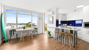 Uma cozinha moderna com vista para o mar, área de refeições com banquetas e uma janela grande.