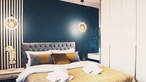 Ein modernes Schlafzimmer mit einer gepolsterten Kopfteile, einem großen Bett mit vielen Kissen, einem Nachttisch mit Blumenvase und zwei Pendelleuchten.