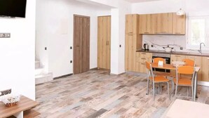 Una cocina moderna con armarios de madera, un comedor con sillas anaranjadas y un televisor de pantalla plana montado en la pared.