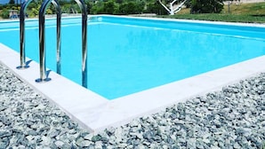 Una piscina rectangular con agua azul cristalina, rodeada por una solana blanca y una zona de grava.