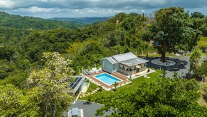 A house with a swimming pool, surrounded by lush greenery and hills.