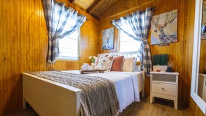 A wooden room with a bed, a nightstand, and a painting on the wall.