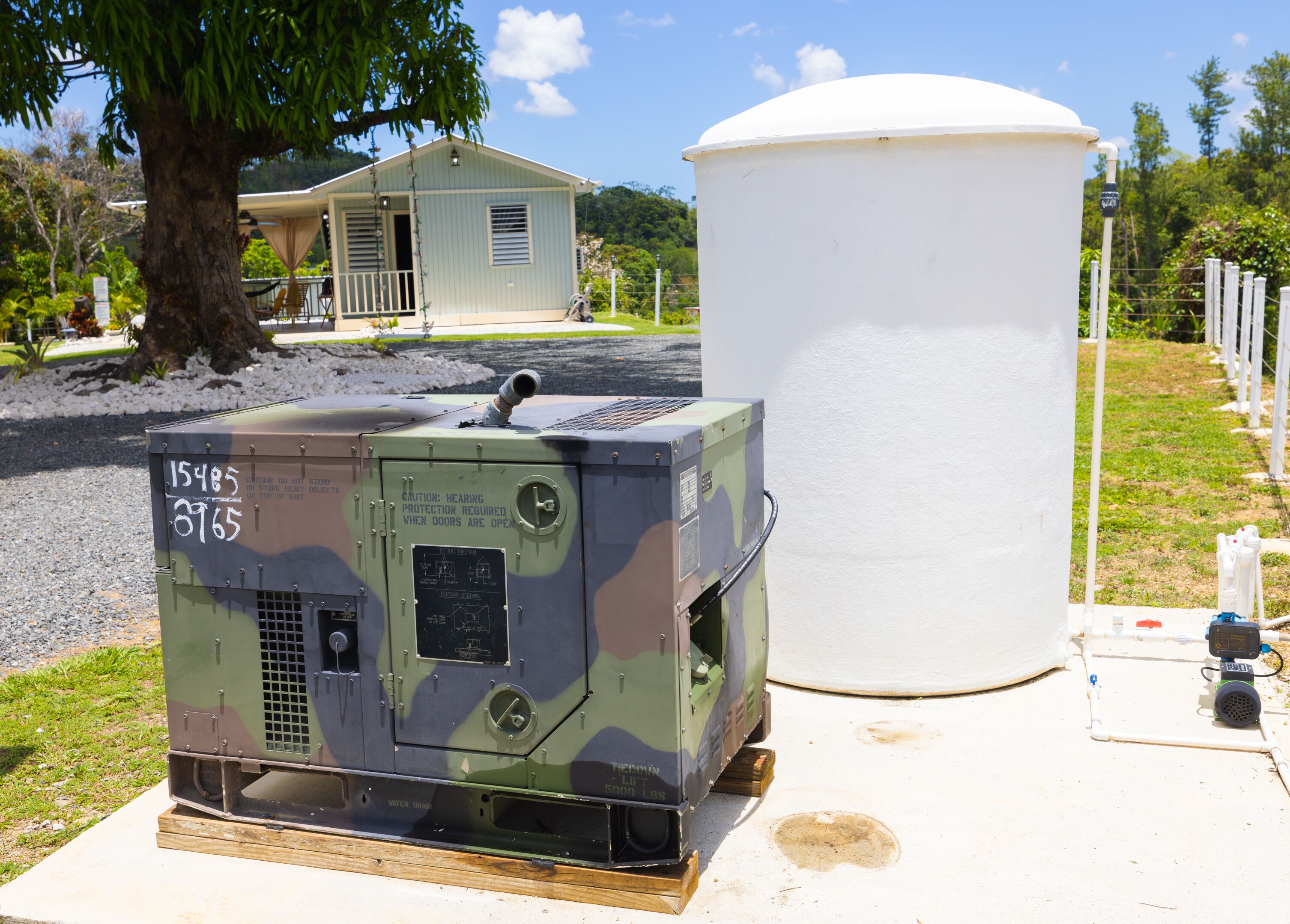 Ein Wassertank und ein Generator auf einem Betonfundament, im Hintergrund ein Haus.