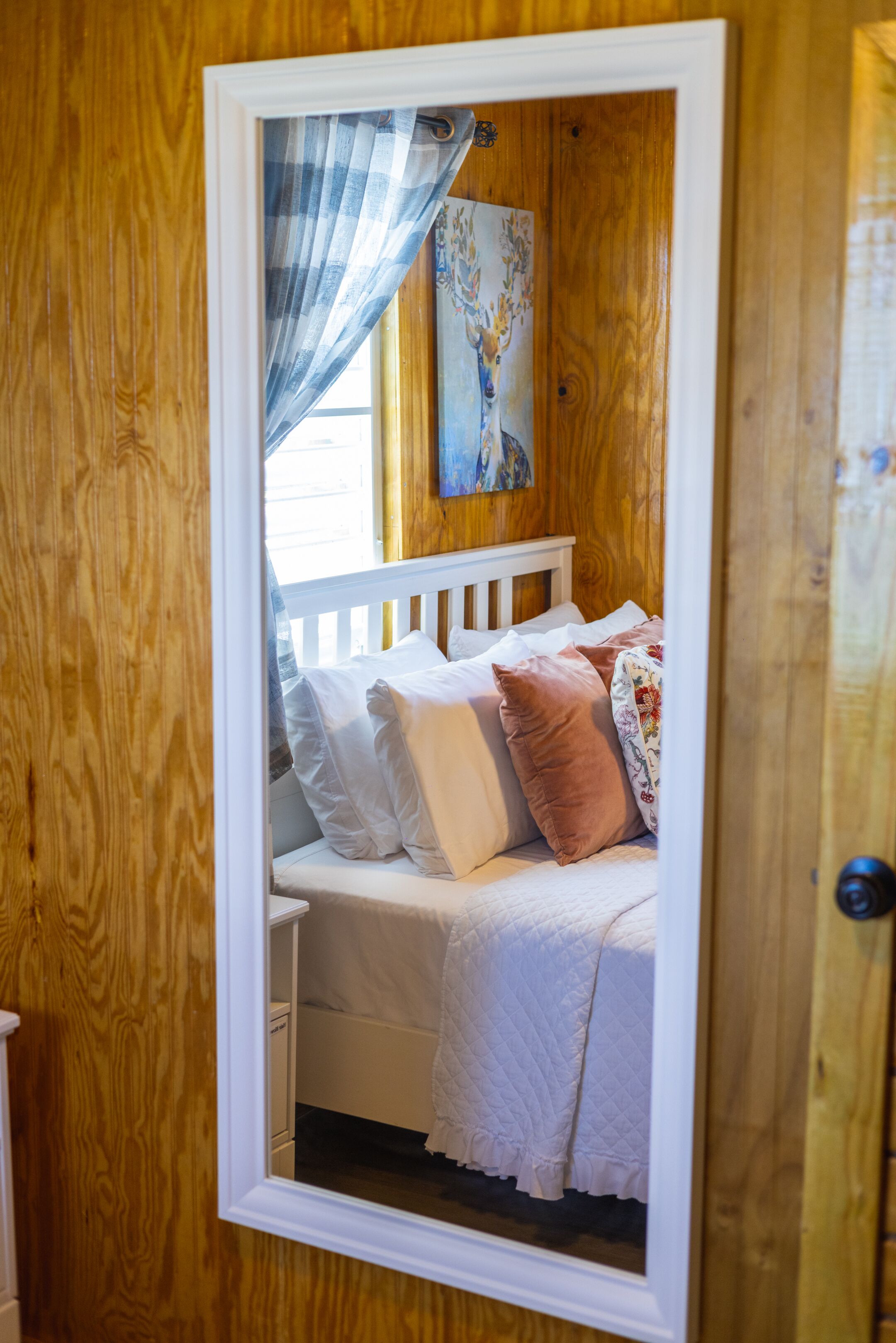 A wooden-paneled room with a bed, white bedding, and a mirror reflecting the room.
