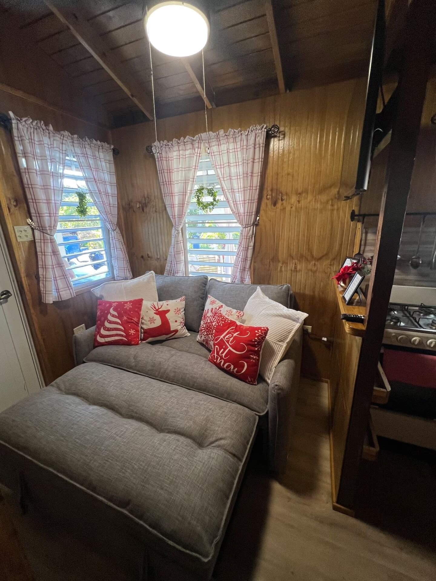 Ein gemütliches Blockhausszimmer mit einem Bett, einer kleinen Küchenzeile und Karo-Vorhängen.