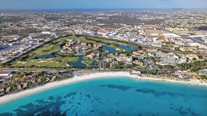 An aerial view of a coastal city with a beach, a golf course, and residential areas.