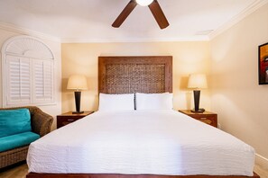 Ein Hotelzimmer mit einem großen Bett, zwei Nachttischen inklusive Lampen, einem Korbsessel und einem dekorativen Kopfteil, sowie einem Deckenventilator.