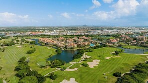 A golf course with a water body, surrounded by residential buildings and a distant mountain range.