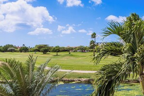 A golf course with a pond, palm trees, and a clear sky.