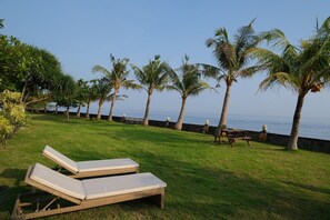 A grassy area with two lounge chairs, palm trees, and a view of the ocean. - Retreat Villa Toraja Baturinggit (Kubu)