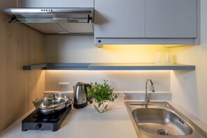 A modern kitchen with a built-in stove, a stainless steel sink, and a compact island with a kettle and a potted plant. - Blue Hippo Hotel (Samut Prakan)