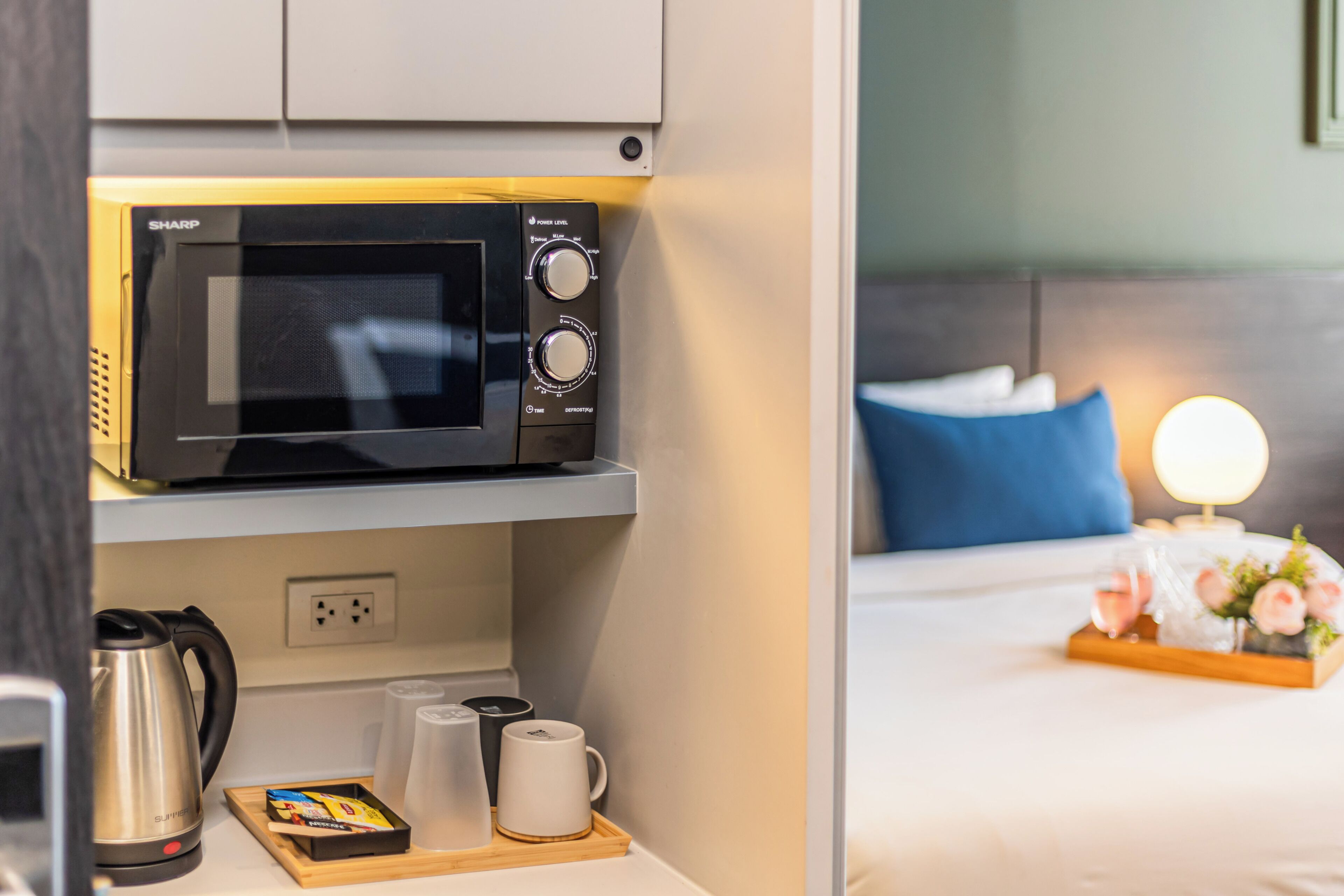 A compact kitchen with a microwave, a kettle, and a tray with cups and a box of tissues.