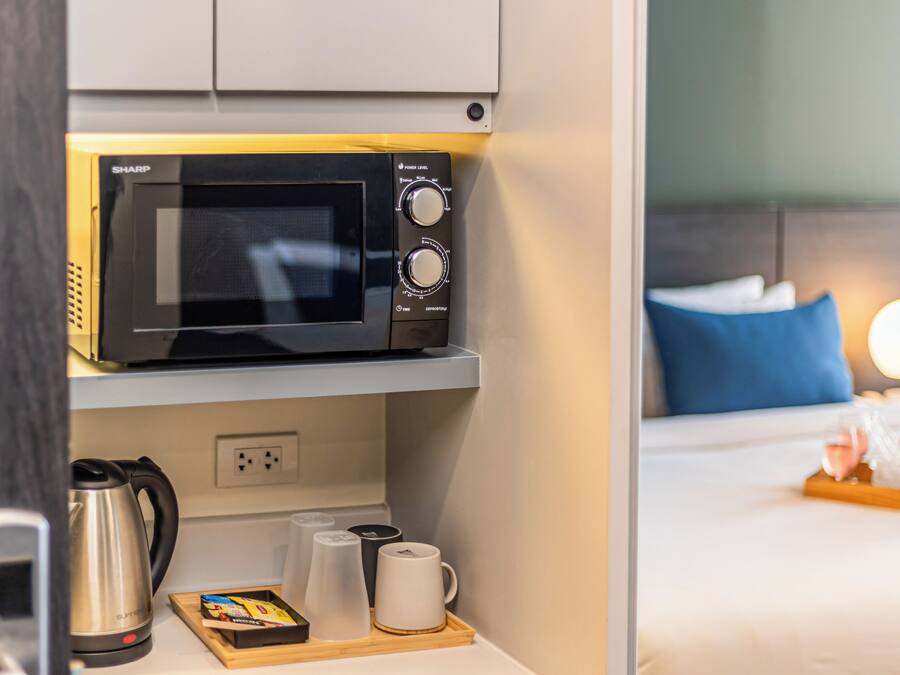 A compact kitchen with a microwave, a kettle, and a tray with cups and a box of tissues.