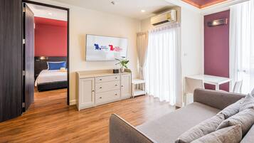 A modern hotel room with a bed, a sofa, a desk, and a TV.