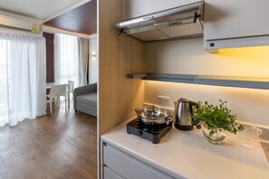 A modern kitchen with a gas stove, a kettle, and a small plant. There is a dining area with a sofa and a table. - Blue Hippo Hotel (Samut Prakan)