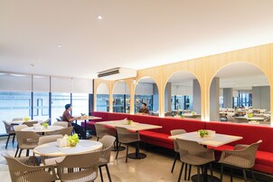 A modern dining area with round tables, red seating, and large windows.