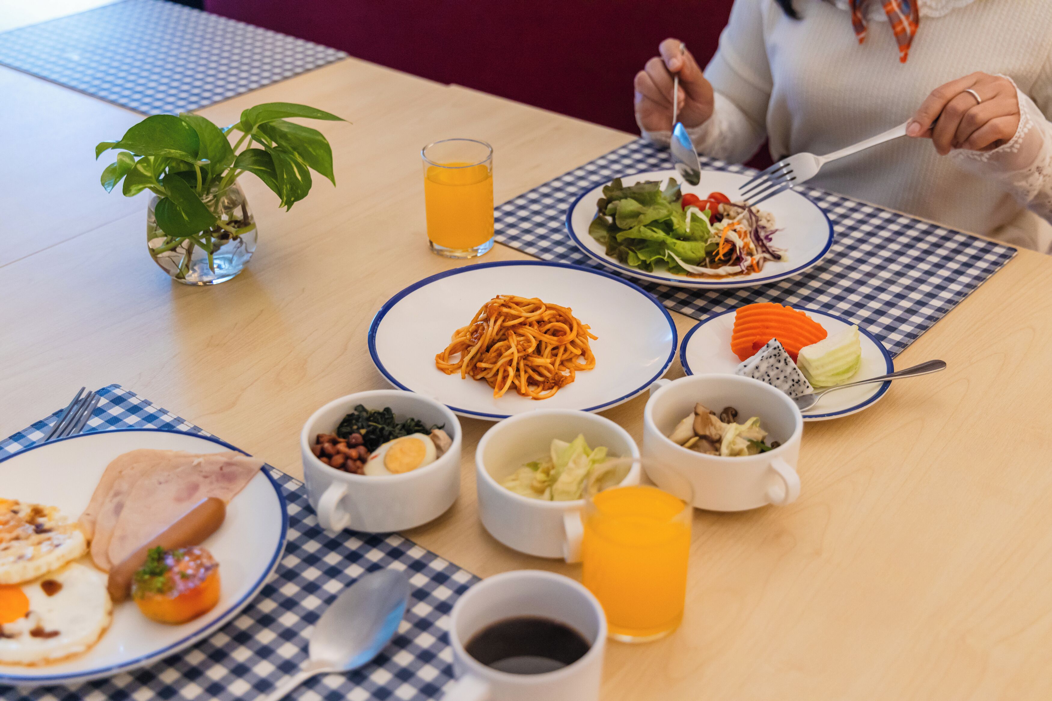 A dining table with various dishes, a glass of orange juice, and a small plant.