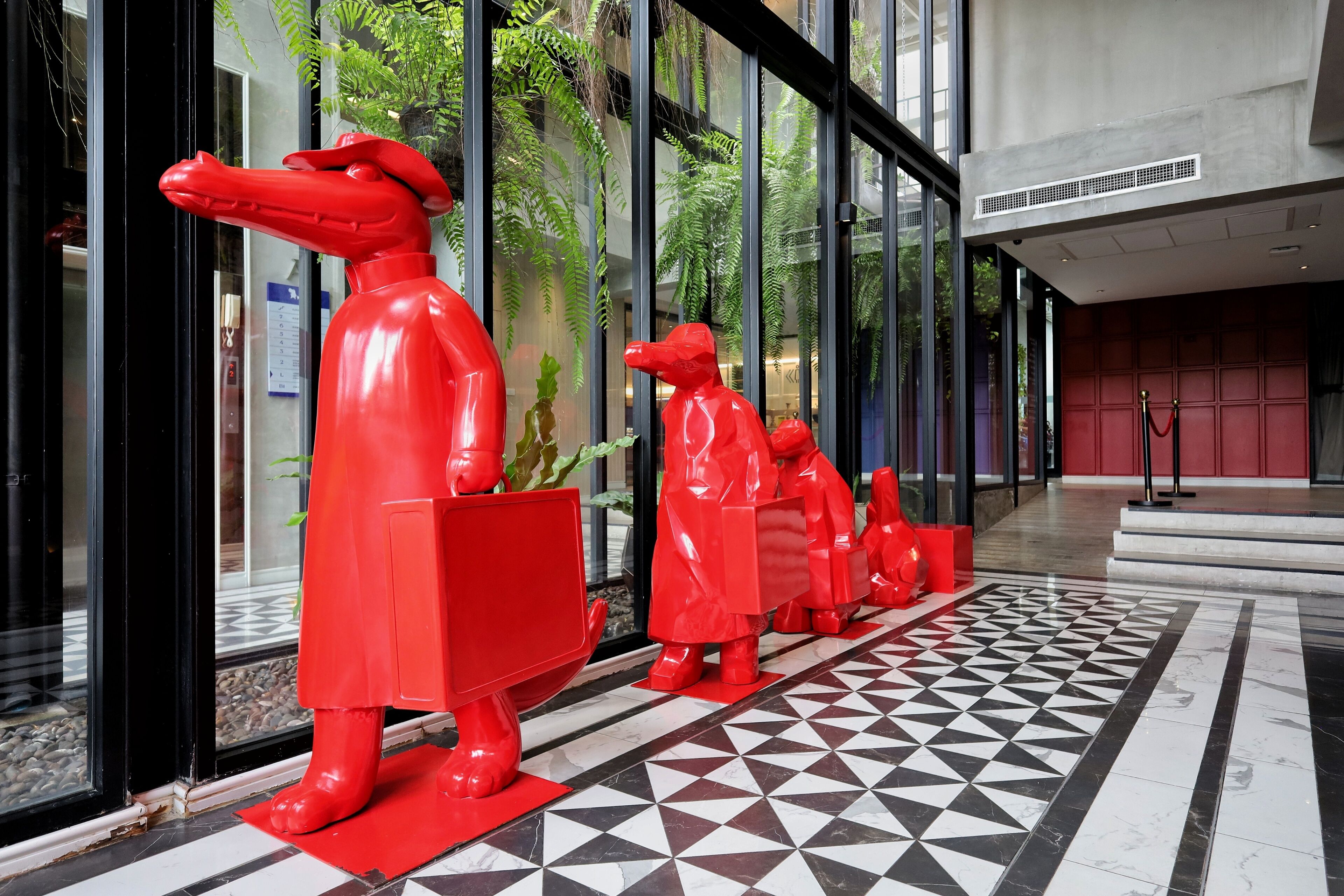 A hallway with a geometric patterned floor, red statues, and glass doors.