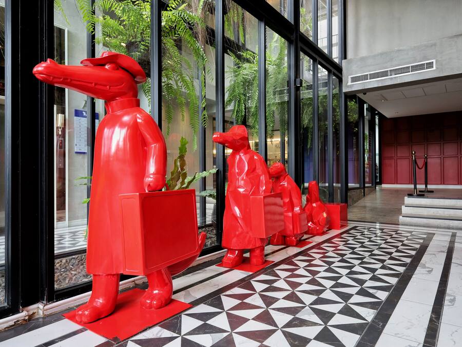 A hallway with a geometric patterned floor, red statues, and glass doors.