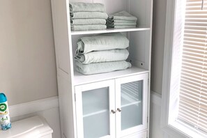 A white cabinet with glass doors and shelves holding folded towels.