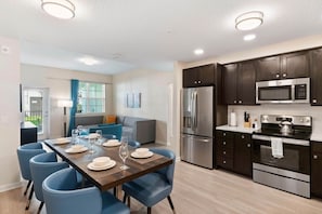 A modern kitchen with dark cabinets, stainless steel appliances, and a dining area with blue chairs and a wooden table set for four. - 3BR Condo w/ Resort Access near OCC, Theme Parks (Orlando)