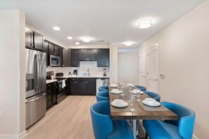 A modern kitchen with stainless steel appliances, a dining area with blue chairs, and a wooden table set for four. - 3BR Condo w/ Resort Access near OCC, Theme Parks (Orlando)