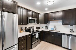 A modern kitchen with dark wood cabinets, stainless steel appliances, and a white countertop. - Resort Condo: 3BR w Balcony & Parking near Disney! (Orlando)