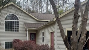 Una casa de un piso con un porche delantero, un garaje y un gran árbol en la fachada.
