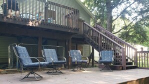 Una terraza de madera con tres sillones azules y una escalera de madera que conduce a un balcón.