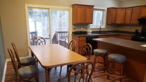 Una cocina con armarios de madera, una mesa de comedor con sillas y vistas a través de puertas correderas de vidrio.