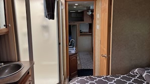 A compact RV interior with a bathroom, kitchenette, and a bed.