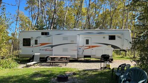 A recreational vehicle (RV) parked in a wooded area with a picnic table and chairs.
