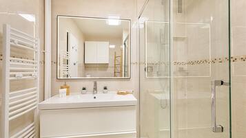Une salle de bain moderne avec une douche à parois de verre, un meuble-lavabo blanc avec un miroir et un porte-serviettes.