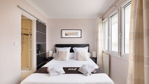 A neatly made bed with white linens, a framed picture above it, and a window with curtains on the right. - Magnificent apartment between Paris and Disneyland. Rer A 10 min by bus -PARKING  (Neuilly-sur-Marne)