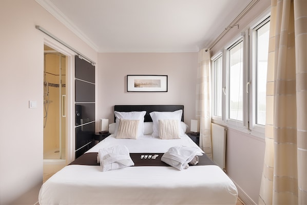 A neatly made bed with white linens, a framed picture above it, and a window with curtains on the right.